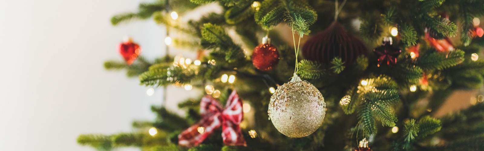 A decorated Christmas tree with lights, ornaments, and red bows. The background is light and out of focus, highlighting the tree's festive decorations.