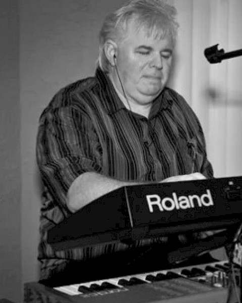 A person is playing a Roland keyboard, using a stand with a mounted device and a microphone.
