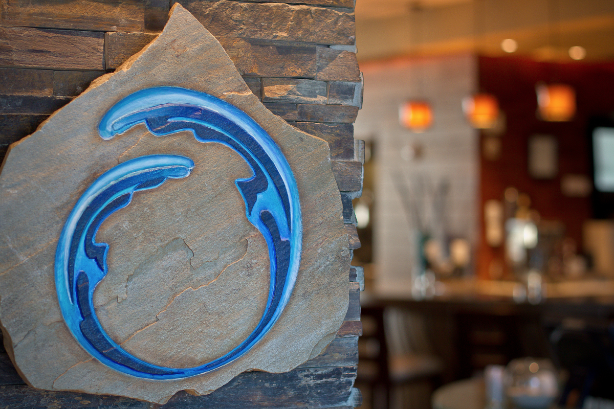The image shows a stone plaque with a blue circular wave design, set against a blurred café or restaurant interior in the background.