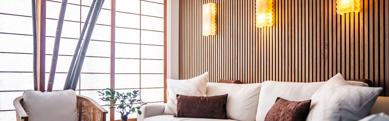 A modern living room with a white sofa, brown cushions, wooden walls, warm lighting, and a small table with a plant.