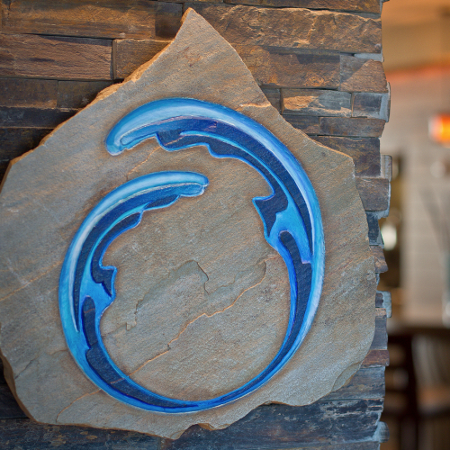 The image shows a stone wall plaque with a blue wave design in front of a blurred indoor setting, possibly a restaurant or bar.