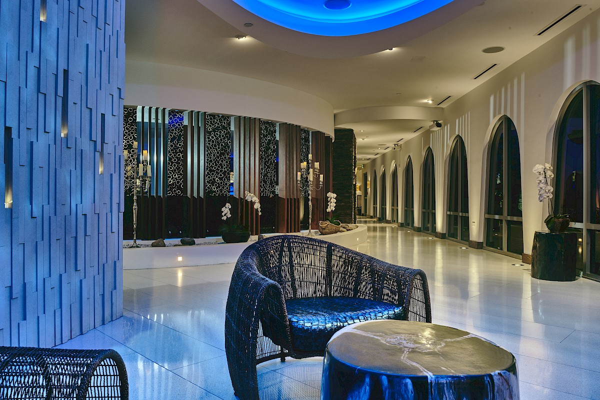 A modern, elegant lobby with curved architecture, blue lighting, wicker chairs, and decorative wall panels.
