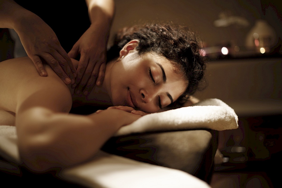A person is receiving a relaxing back massage in a dimly lit, tranquil setting, lying on a massage table with towels.