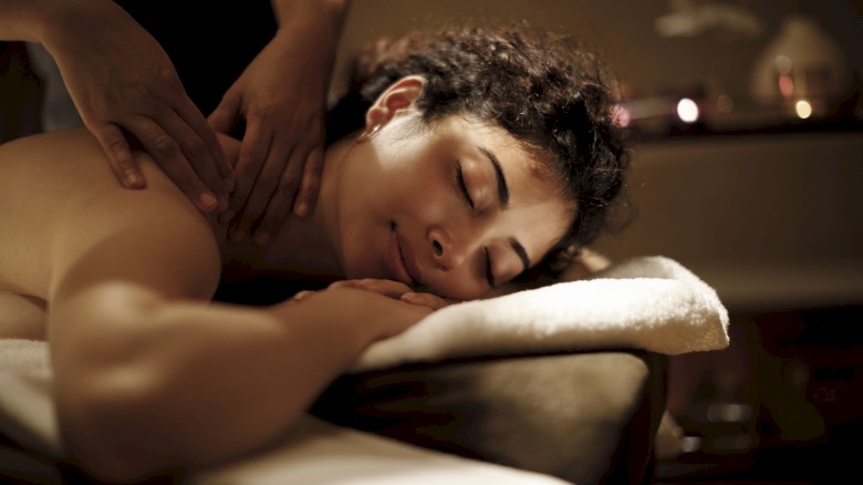 A person is receiving a relaxing back massage in a dimly lit, tranquil setting, lying on a massage table with towels.