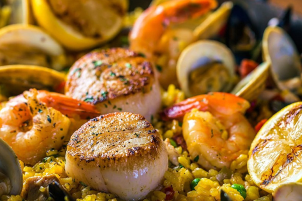 A vibrant seafood paella with shrimp, scallops, clams, and grilled lemon slices on a bed of yellow rice, garnished with herbs.