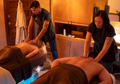 Two people receiving massages in a cozy room, with therapists providing treatment under warm lighting.